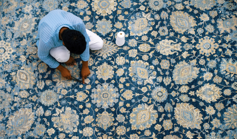 Artisan handcrafting a blue floral luxury rug with intricate patterns and golden accents